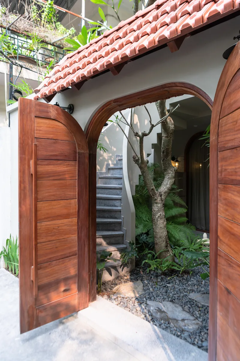 Arched timber doorway opening to a courtyard with terrazzo flooring, planted tree, and terracotta tile roof