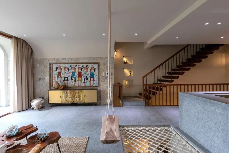 Double-height living space with timber staircase, terrazzo island, and glass floor panel revealing lower level