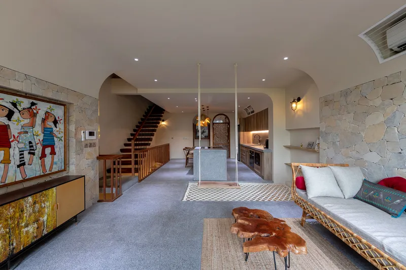 Open-plan living space with stone walls, timber staircase, and rope hammock under recessed ceiling light