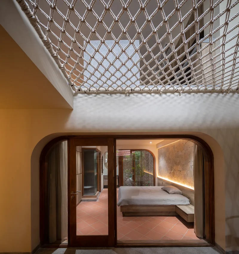 View through rounded timber doorway to bedroom with rope net skylight overhead