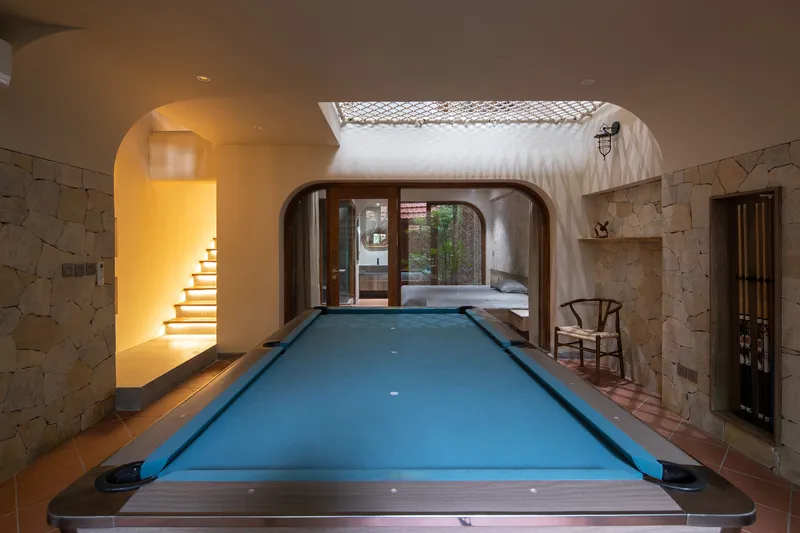 Billiard table beneath rope net skylight with view through arched opening to bedroom beyond