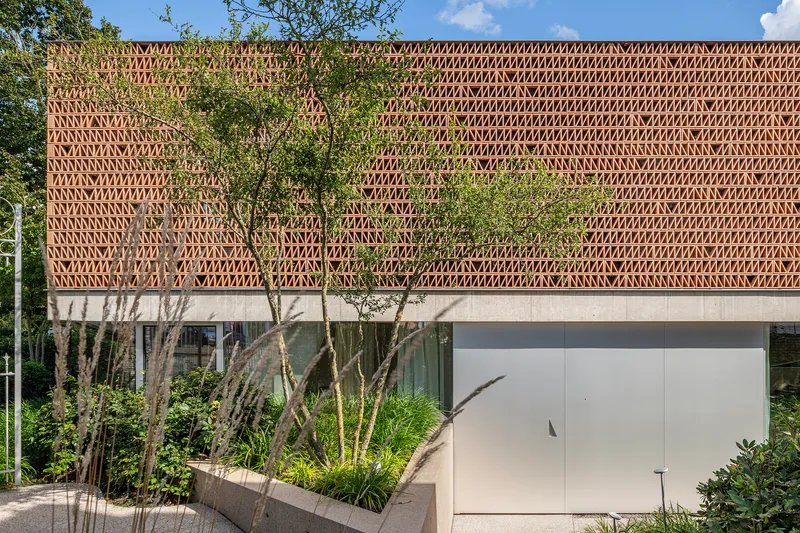 Perforated brick facade with young trees and planted beds in summer sunlight