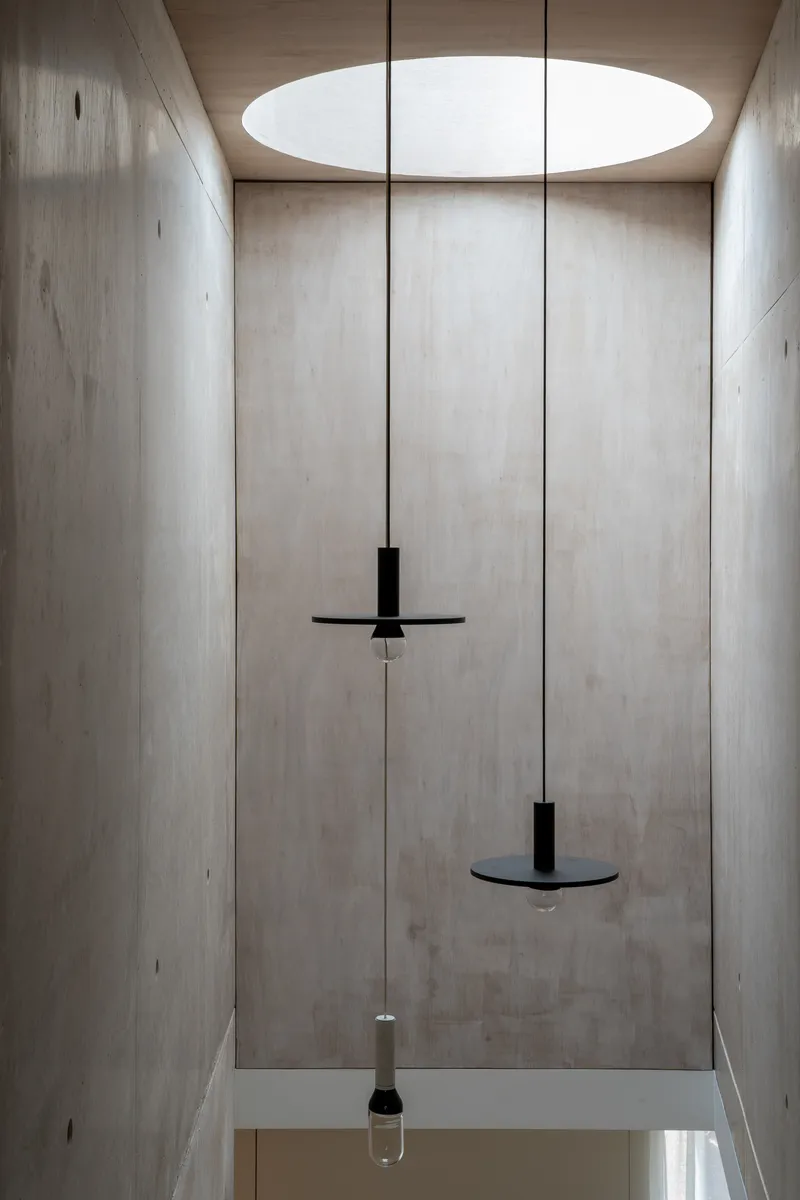 Double-height concrete stairwell with circular skylight and suspended black pendant fixtures