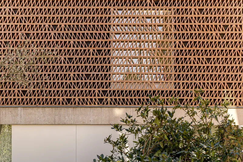 Timber lattice facade with diagonal bracing pattern above planted garden beds at dusk