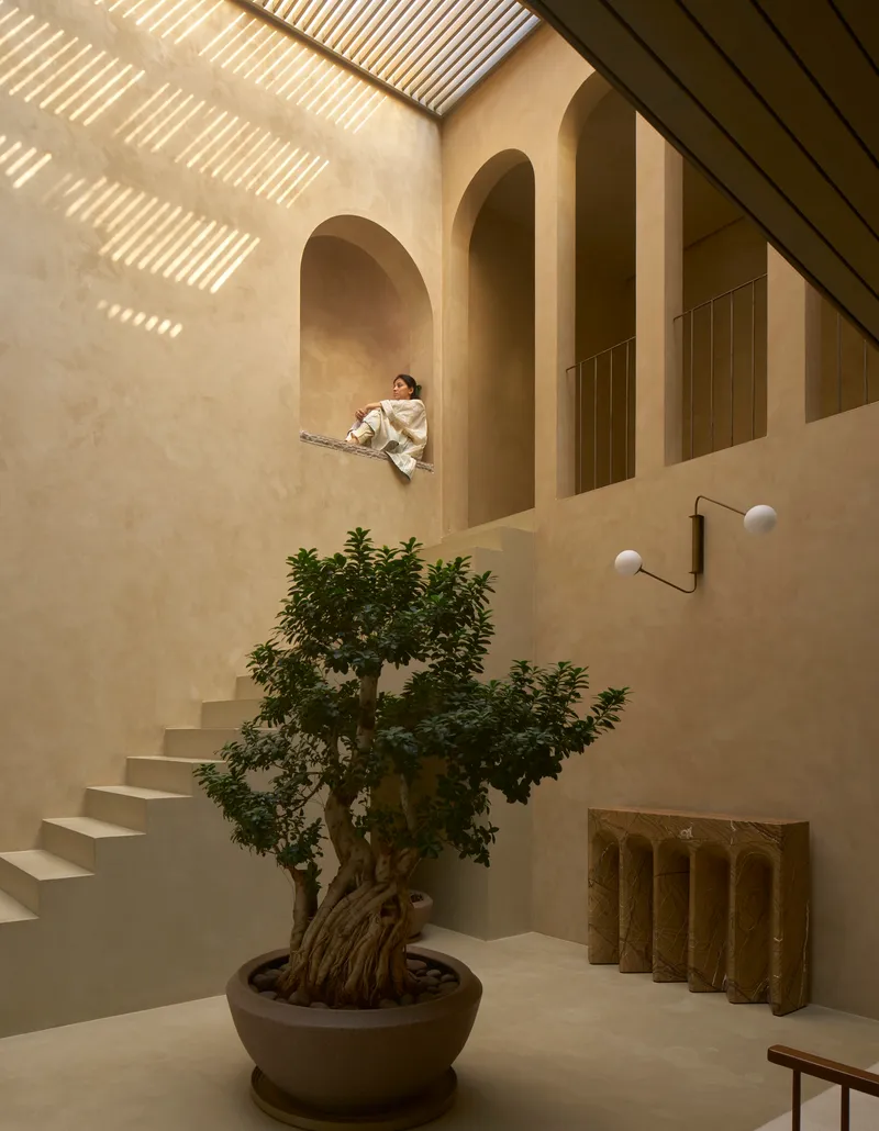 Multi-level courtyard with arched openings, floating stairs, and a person seated in an alcove above
