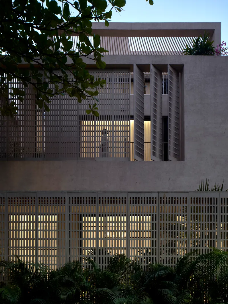 Street view of stacked volumes with brise-soleil screens and planted foreground at twilight