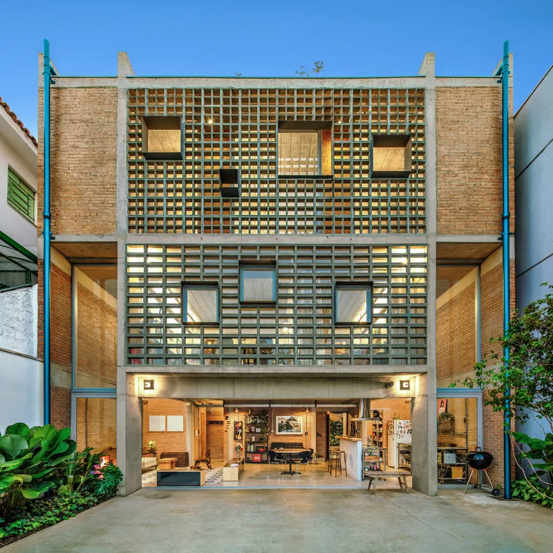 Street facade with perforated concrete block screen and open ground floor beneath a clear blue sky