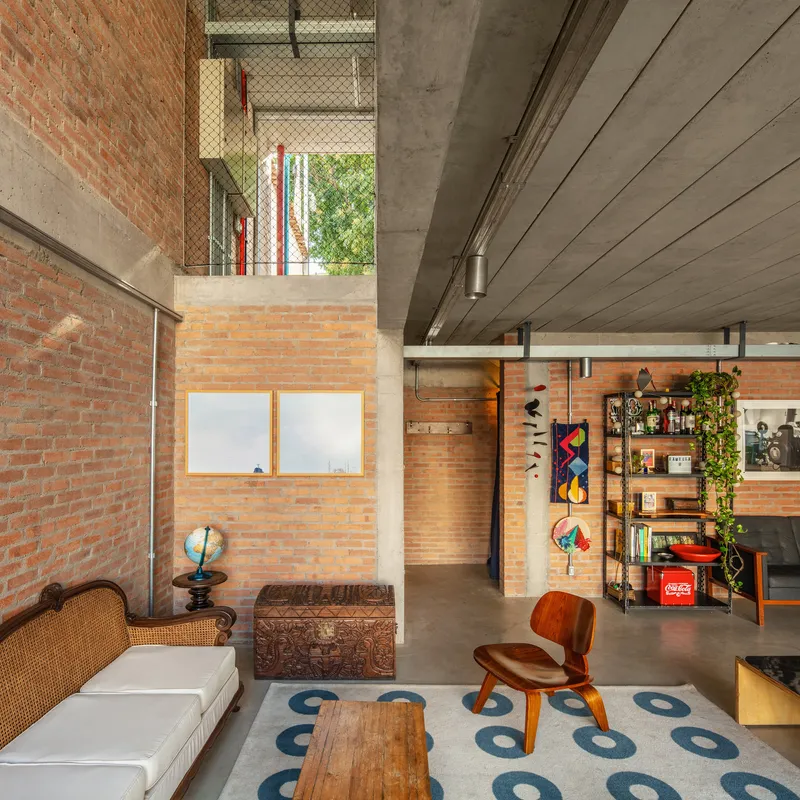 Double-height living space with exposed brick walls and concrete ceiling looking up toward a terrace