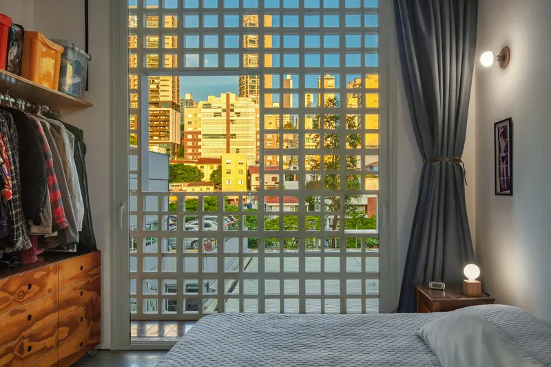 Bedroom with concrete block screen wall filtering warm evening light from the urban skyline
