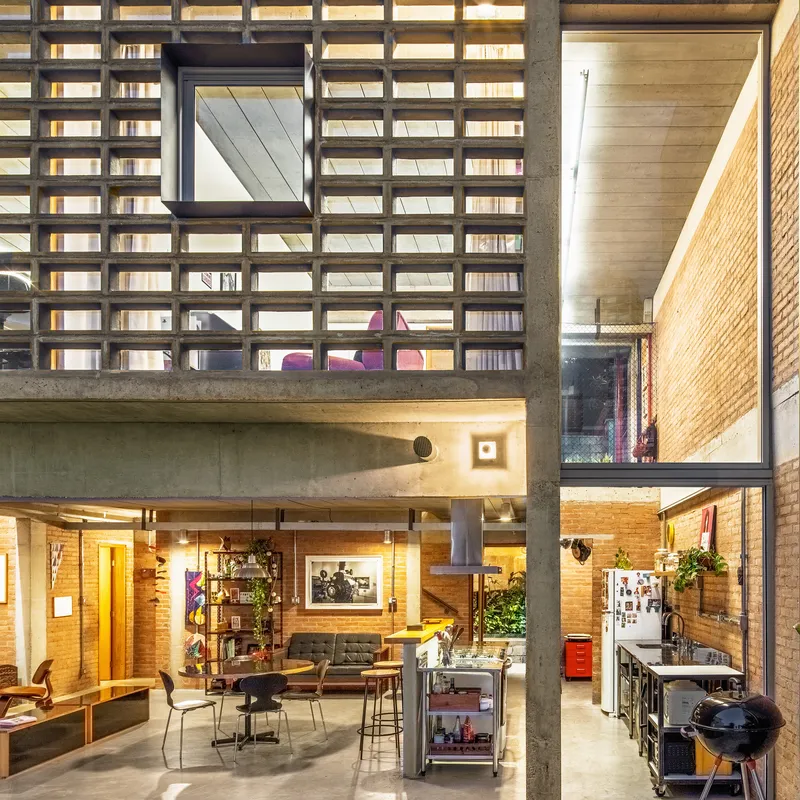 Double-height interior showing concrete columns, brick walls, and grid screen facade lit at dusk