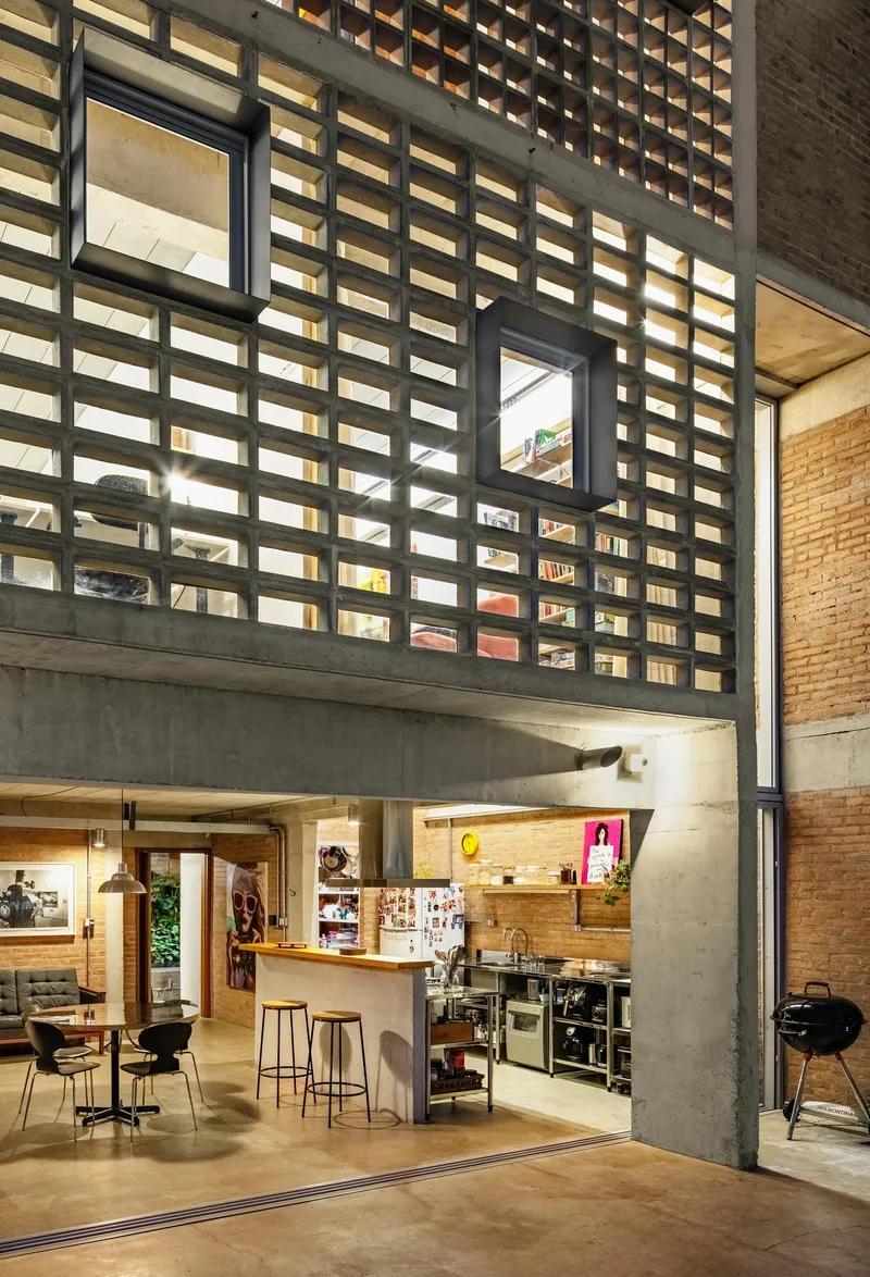 Kitchen area beneath concrete grid screen with framed openings and brick walls in warm artificial light