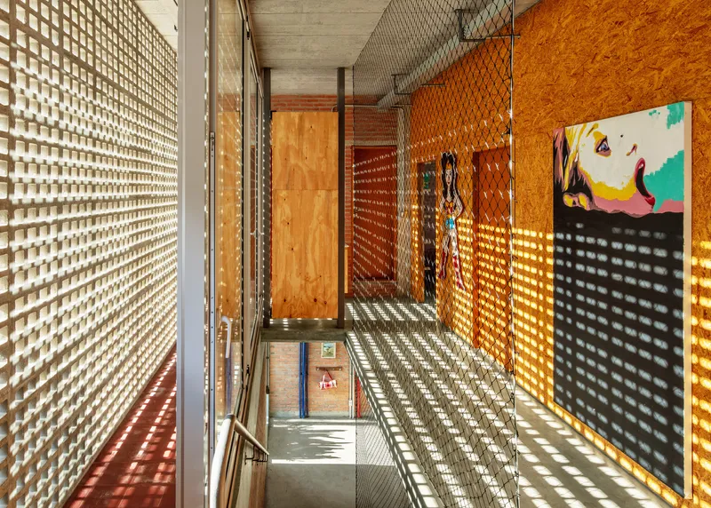 Stairwell with perforated block walls casting latticed shadow patterns across plywood panels and concrete floor