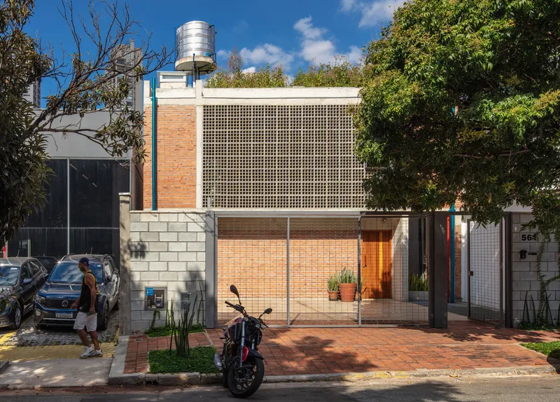 Street facade with perforated concrete block screen and brick walls framed by trees and parked cars