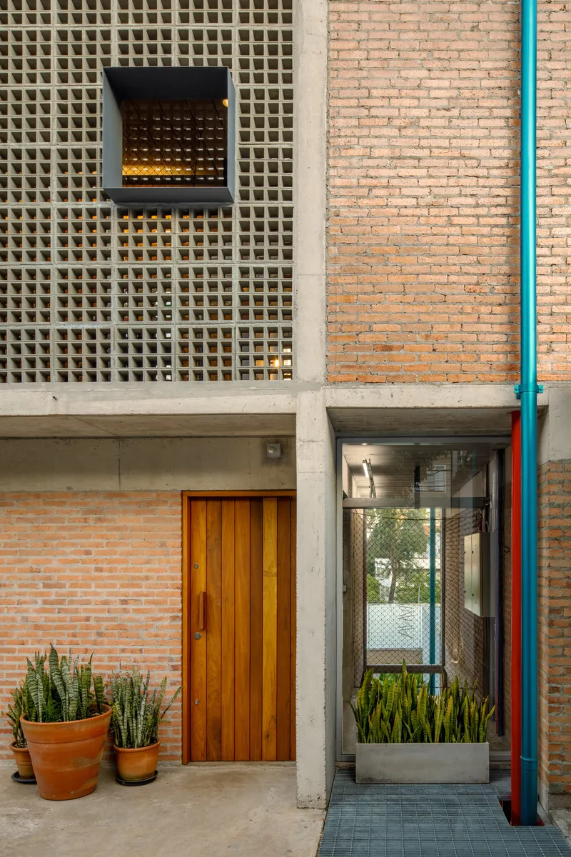 Close-up of facade showing black window frame set into perforated concrete block wall beside brick