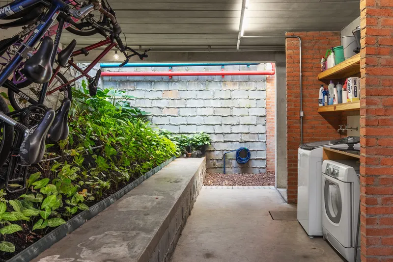 Interior courtyard with planted bed along white brick wall and bicycles hung on corrugated metal ceiling
