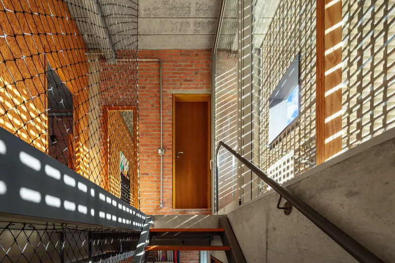 Stairwell with concrete steps and chain link mesh guard panels casting patterned shadows on brick wall