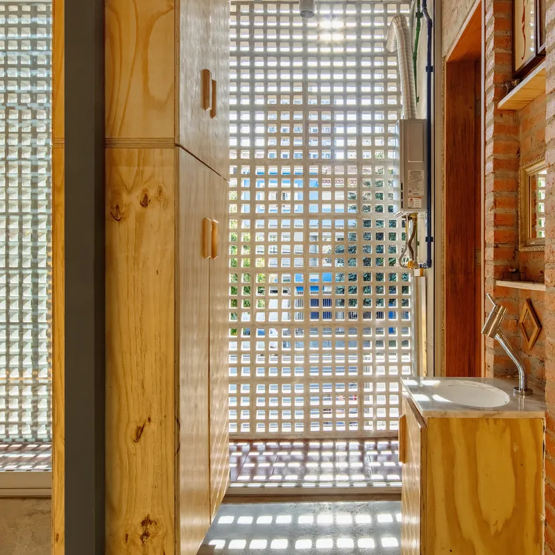 Bathroom corridor with glass block wall filtering daylight onto plywood cabinetry and concrete floor