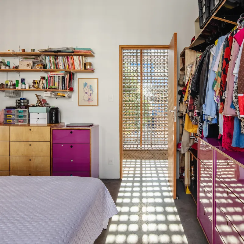 Bedroom with glass block door casting grid shadows across concrete floor and open wardrobe