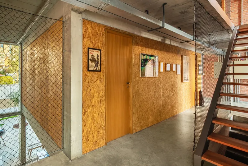 Upper hallway with oriented strand board wall and chain link mesh stair railing