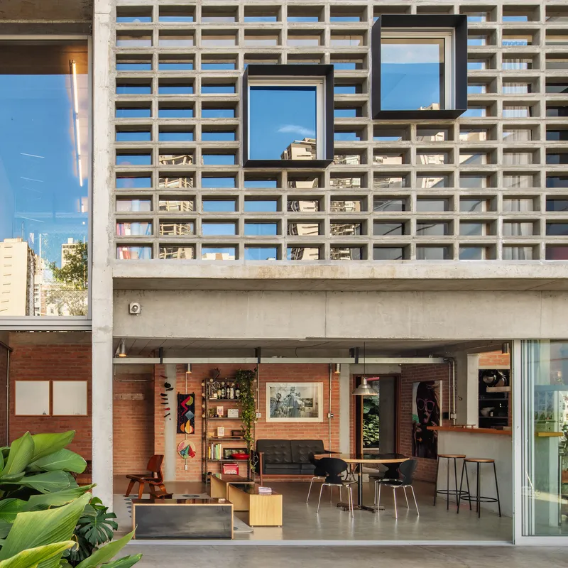 Open-air ground floor with exposed brick walls and concrete breeze block screen above under a clear blue sky