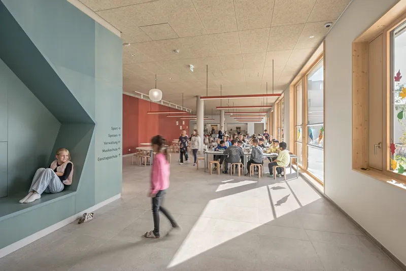 Dining hall with acoustic ceiling panels and suspended red linear lighting above children at tables