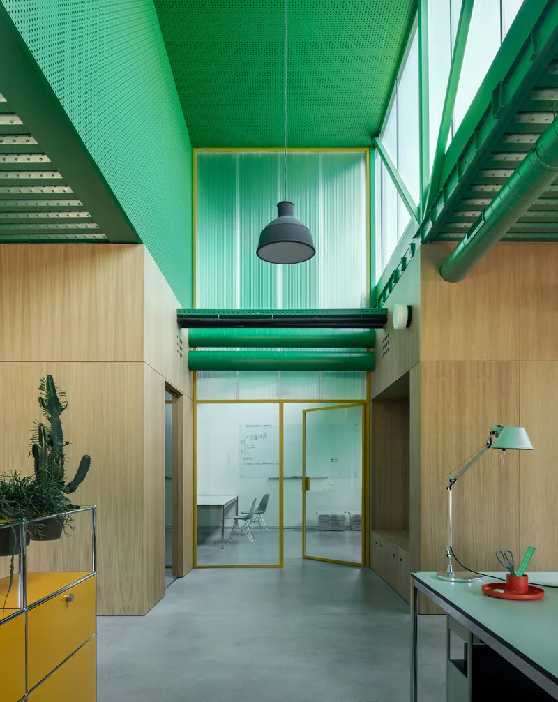 Double-height interior workspace with exposed green steel trusses and yellow-framed glazing under clerestory windows