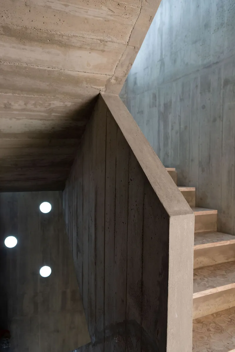 Board-formed concrete staircase ascending alongside a vertical wall with three circular light fixtures