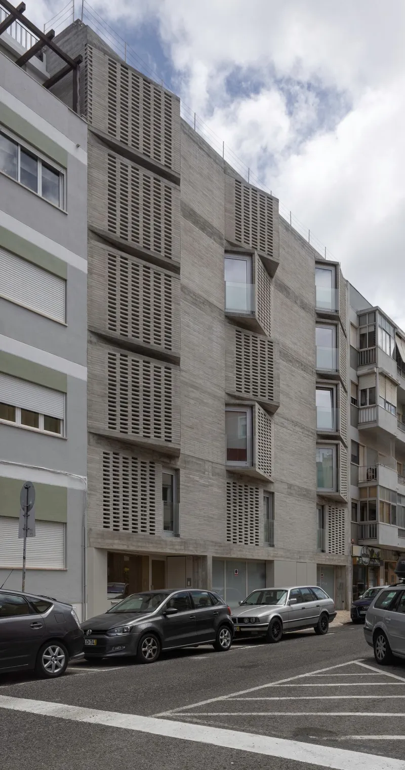 Full elevation showing alternating concrete and perforated screen panels beside parked cars on the street below