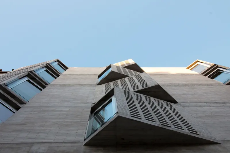 Worm's-eye view of angled bay windows and louvered sunscreens projecting from the concrete facade against clear blue sky