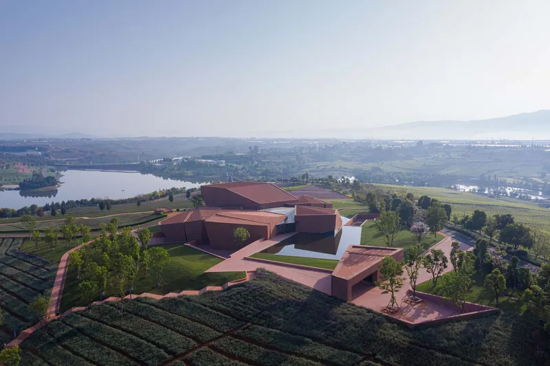 Aerial view of clustered red brick volumes surrounded by terraced gardens and agricultural fields