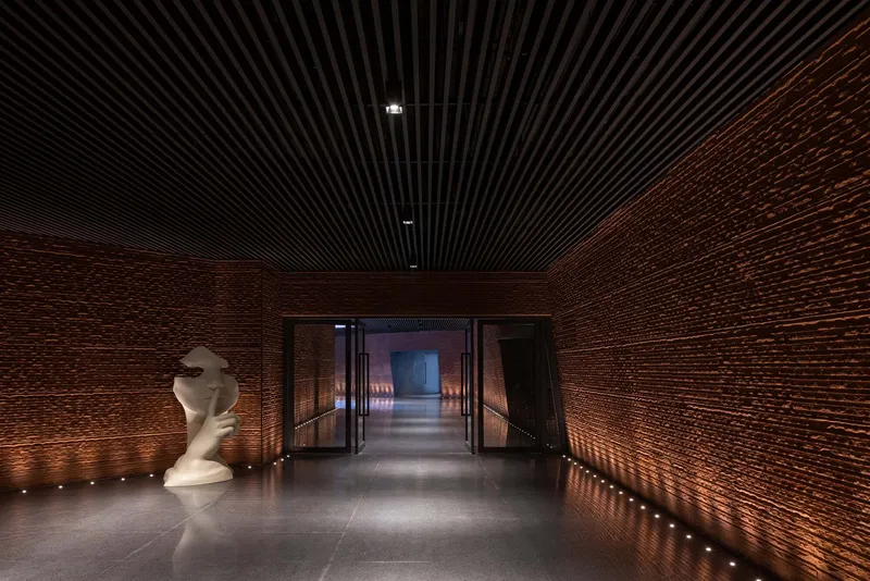 Entry corridor with glazed doors flanked by brick walls and sculpture under a linear black ceiling