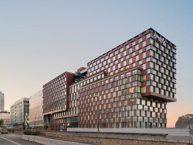 Street view of the chequered red and white panel facades arranged in stacked volumes at dusk