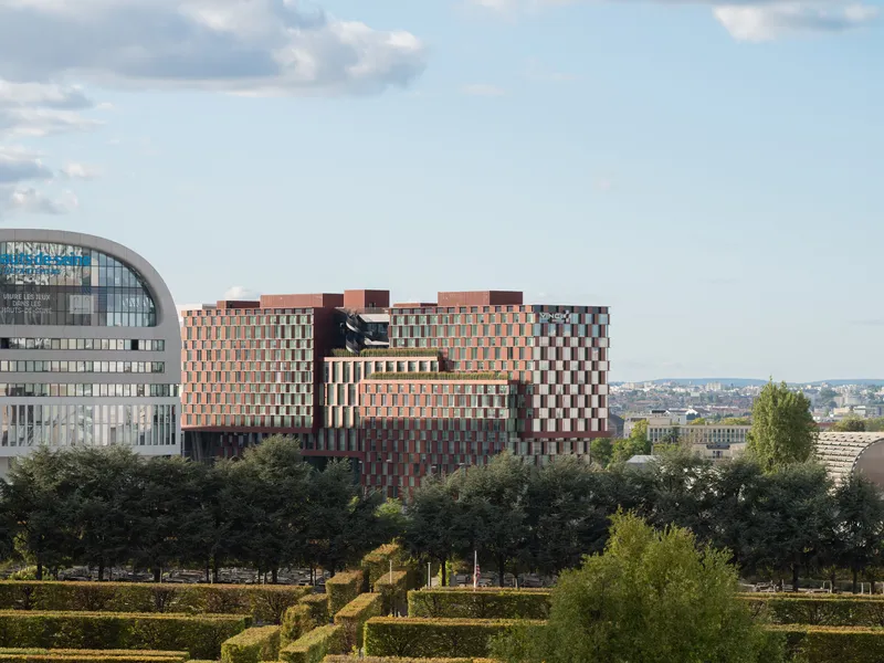 Distant view of the multi-volume facade rising above a landscaped foreground with mature trees