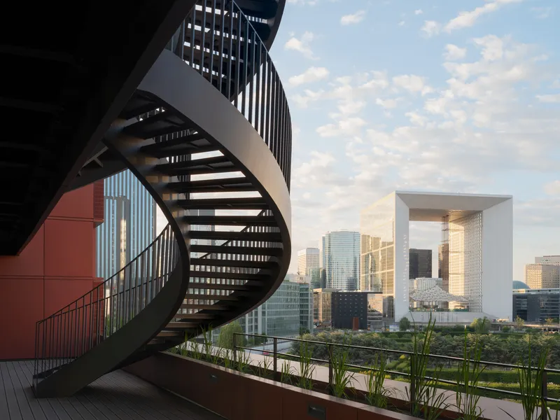 Rooftop terrace with curved steel staircase and planters overlooking the skyline in afternoon light