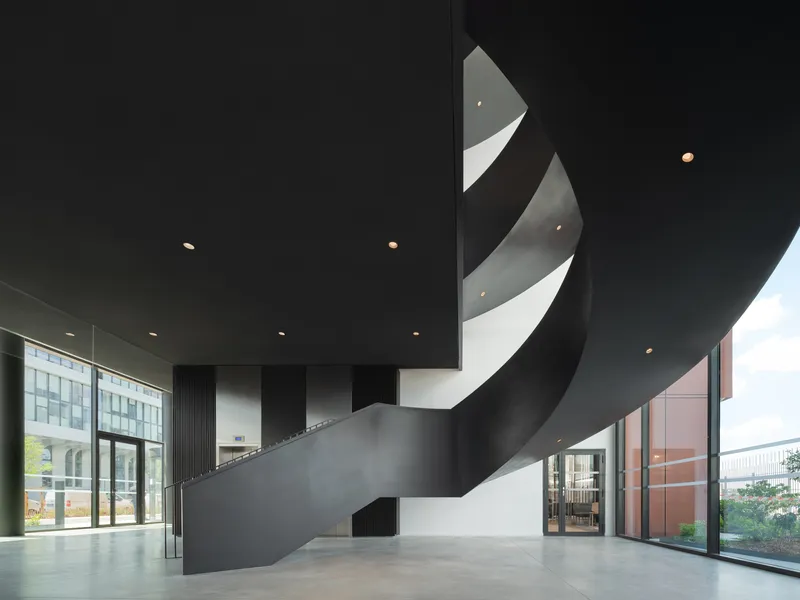 Interior lobby with black ribbon staircase spiraling beneath recessed ceiling downlights and glazed walls
