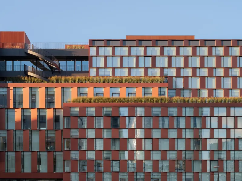 Chequered facade of terracotta and glass panels with rooftop planted terraces under a clear blue sky