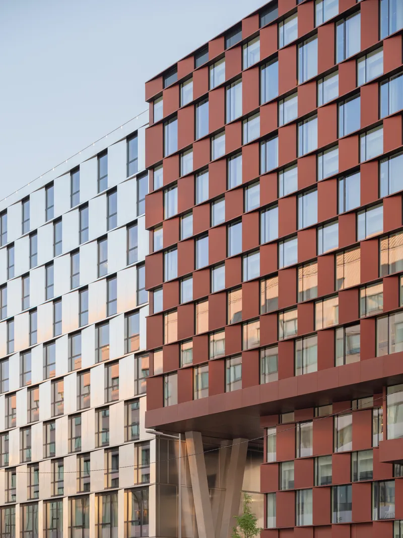 Cantilevered volume supported by angled concrete columns beneath a gridded terracotta and glass facade at dusk