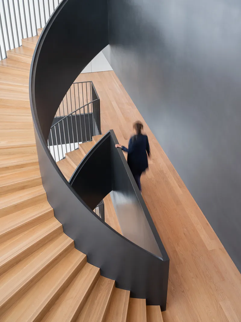 Top-down view of a curving timber staircase with black steel balustrade and a person descending