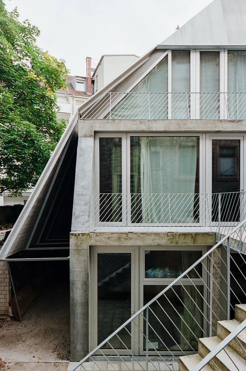 Concrete rear facade with diagonal bracing, glazed balconies, and metal stair connecting courtyard levels