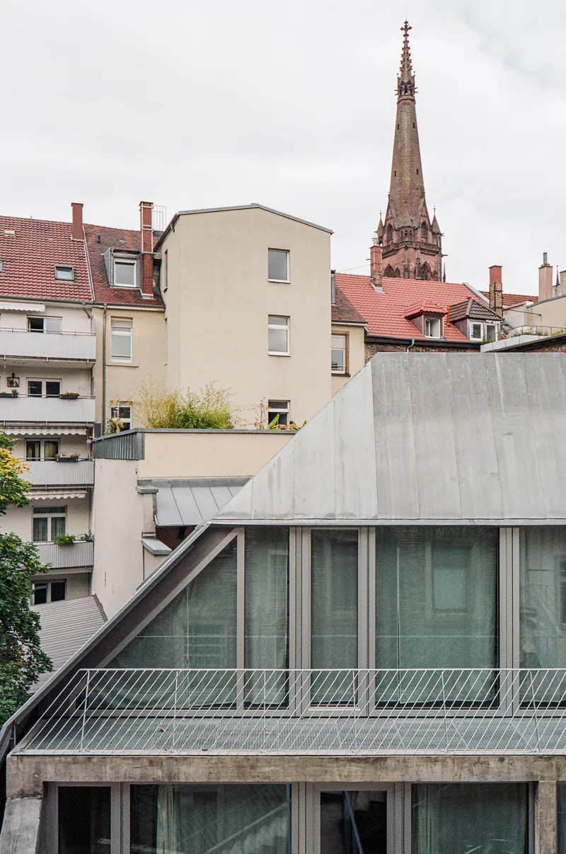 Rooftop view of the angled concrete volume with metal railings against a church spire beyond