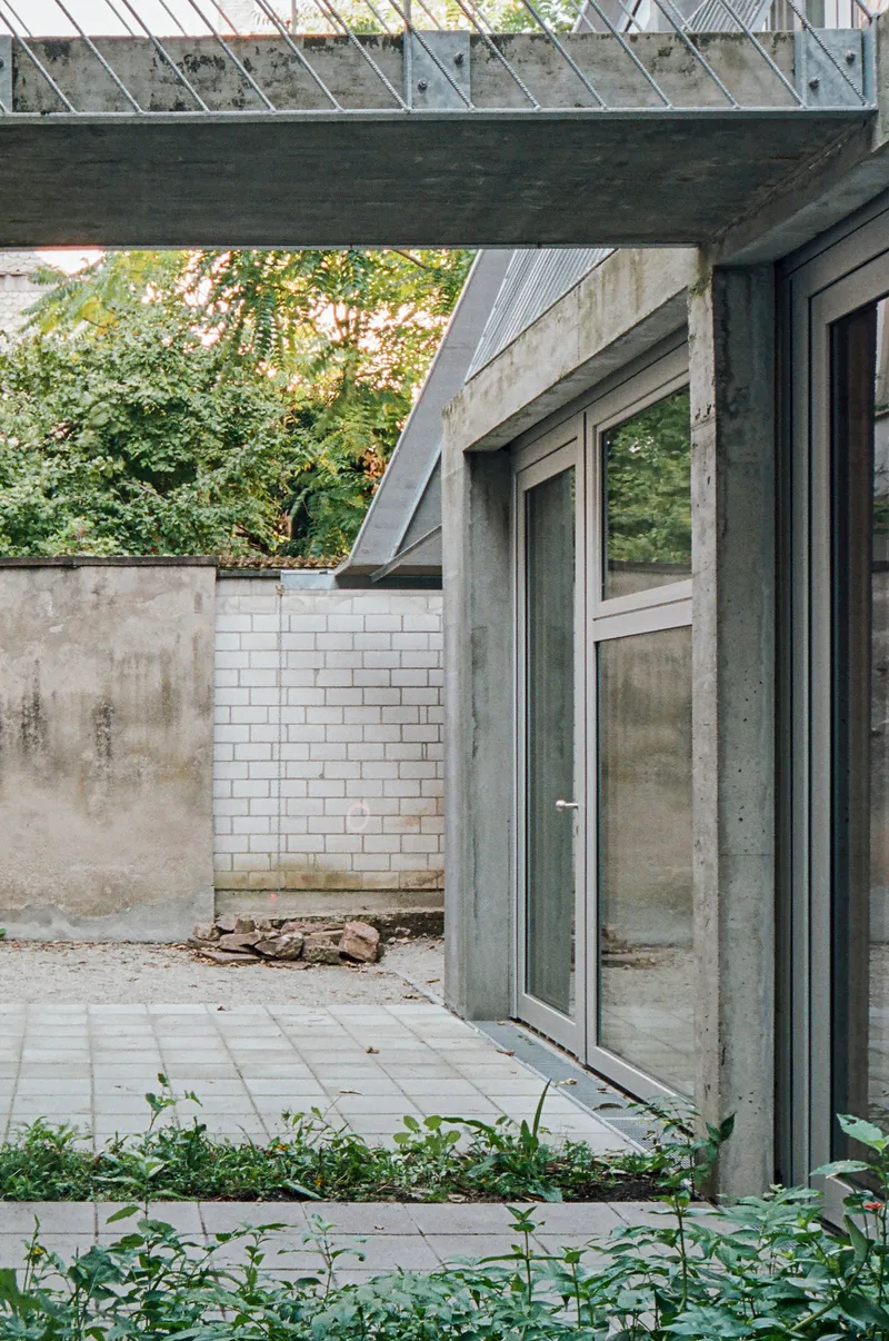 Courtyard terrace with concrete doorframe, white brick wall, and overhead metal grating in afternoon light