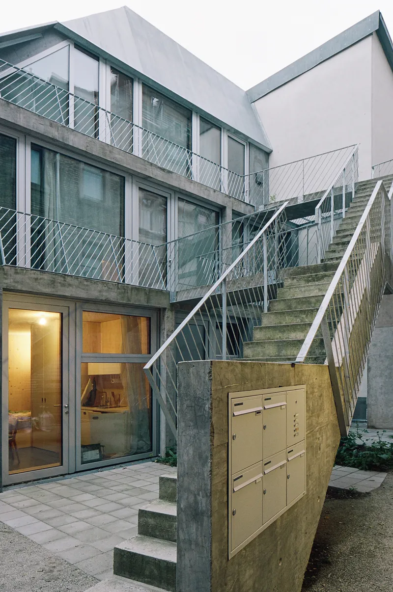 Concrete exterior staircase with white diagonal railings ascending through courtyard between balconies and mailbox