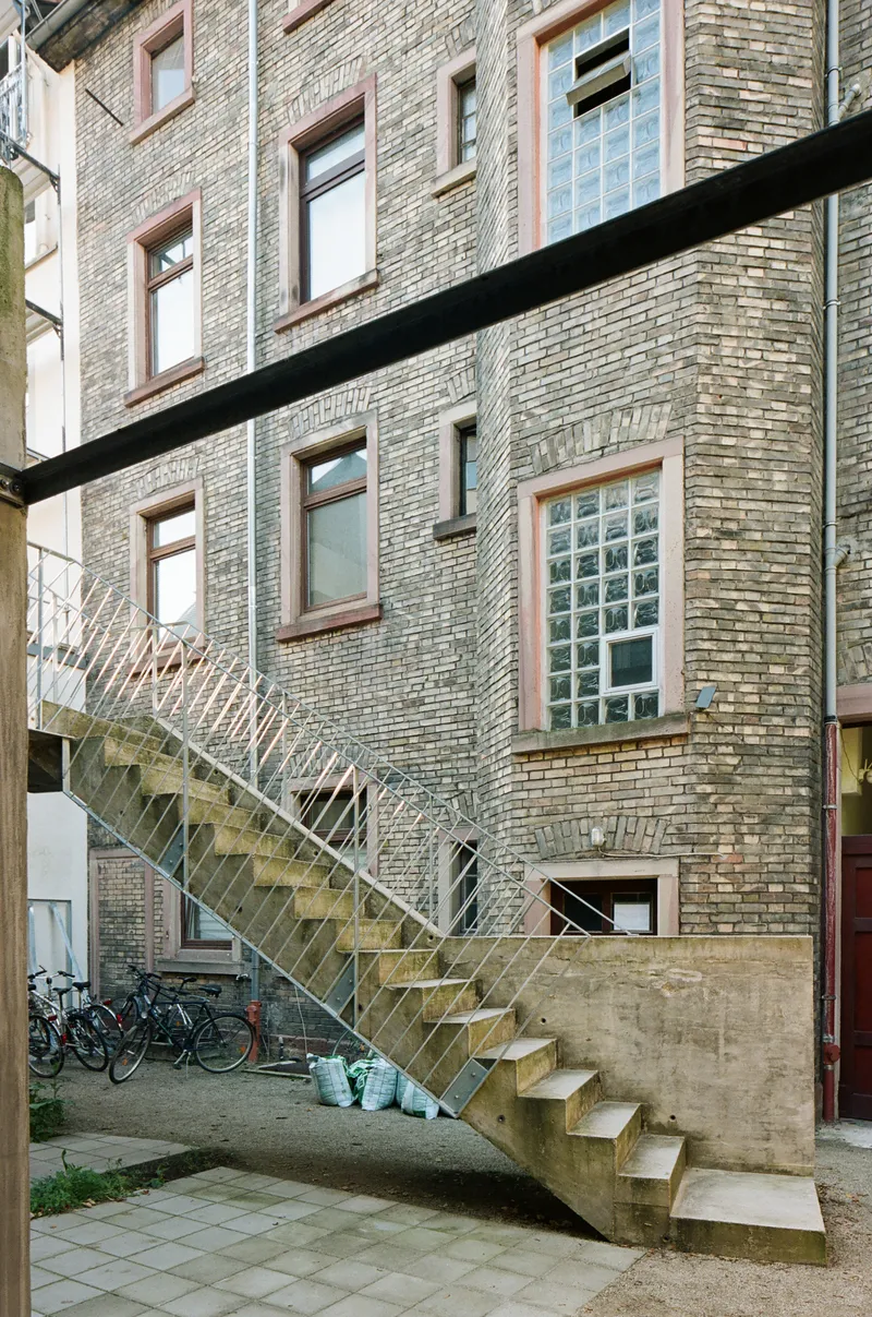 Exterior steel staircase ascending concrete base against grey brick wall with parked bicycles below