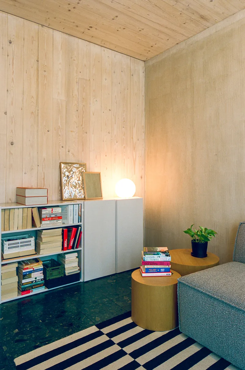 Reading nook corner with plywood wall paneling, low shelving, sphere lamp and striped rug on terrazzo