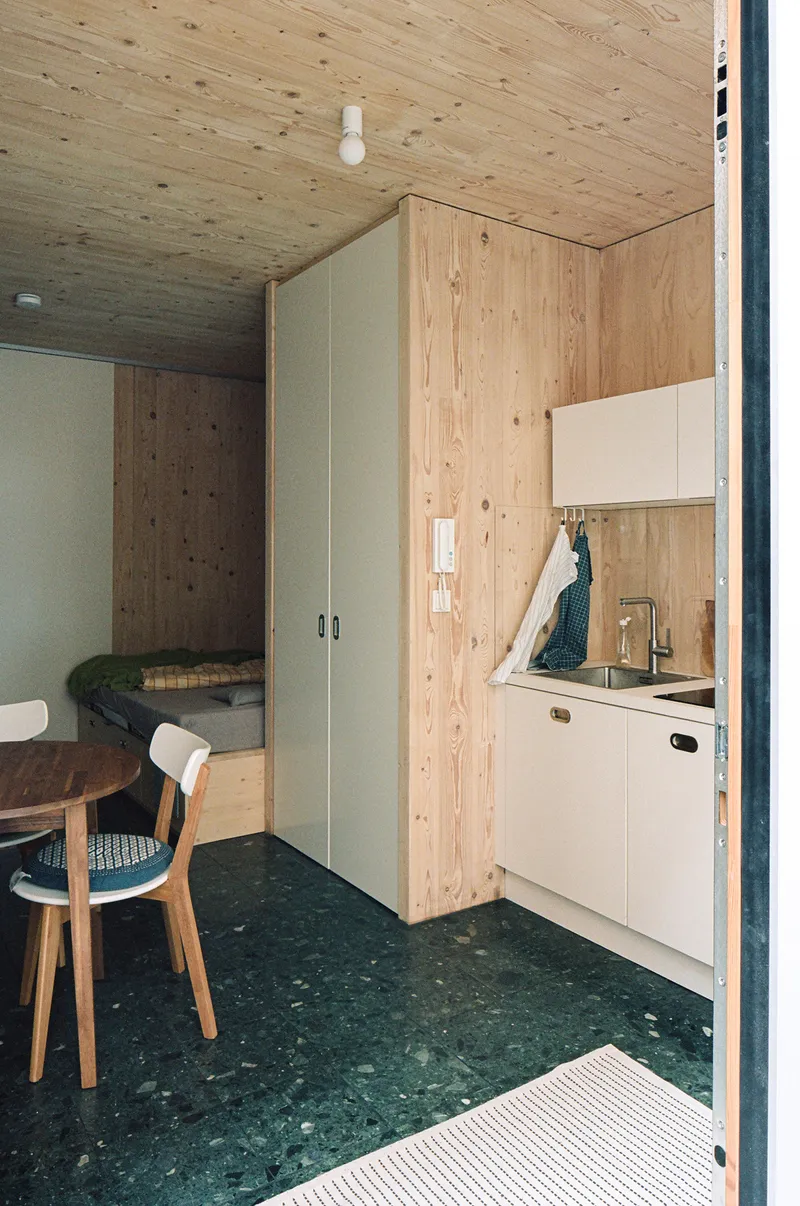 Compact kitchenette with white cabinetry and sink tucked into plywood wall beside tall storage unit