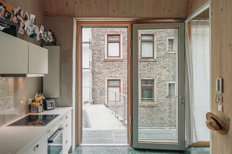 Kitchen opening through timber-framed glass doors onto a metal grate terrace overlooking a brick courtyard