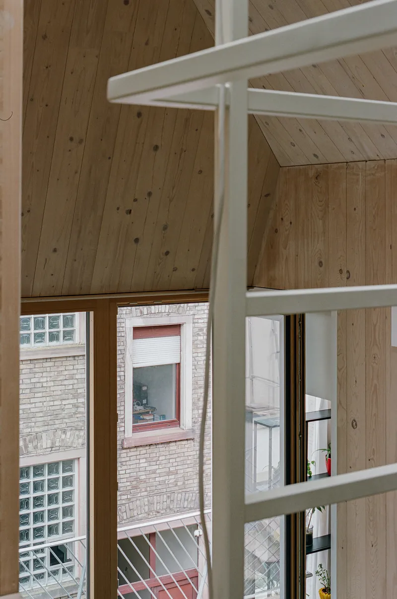 White steel ladder frame against exposed timber plank ceiling and window overlooking neighboring brick facade