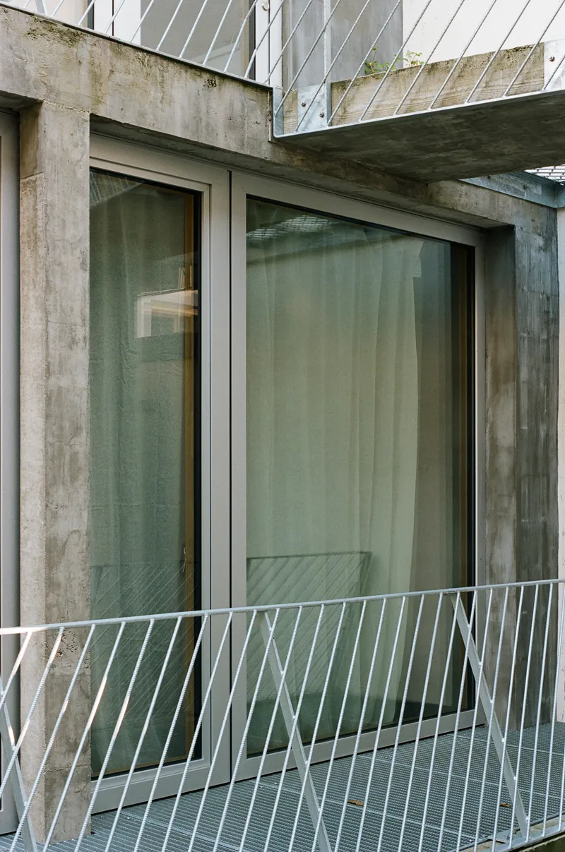 Concrete balcony threshold with glass sliding doors and white diagonal balustrade against weathered concrete walls
