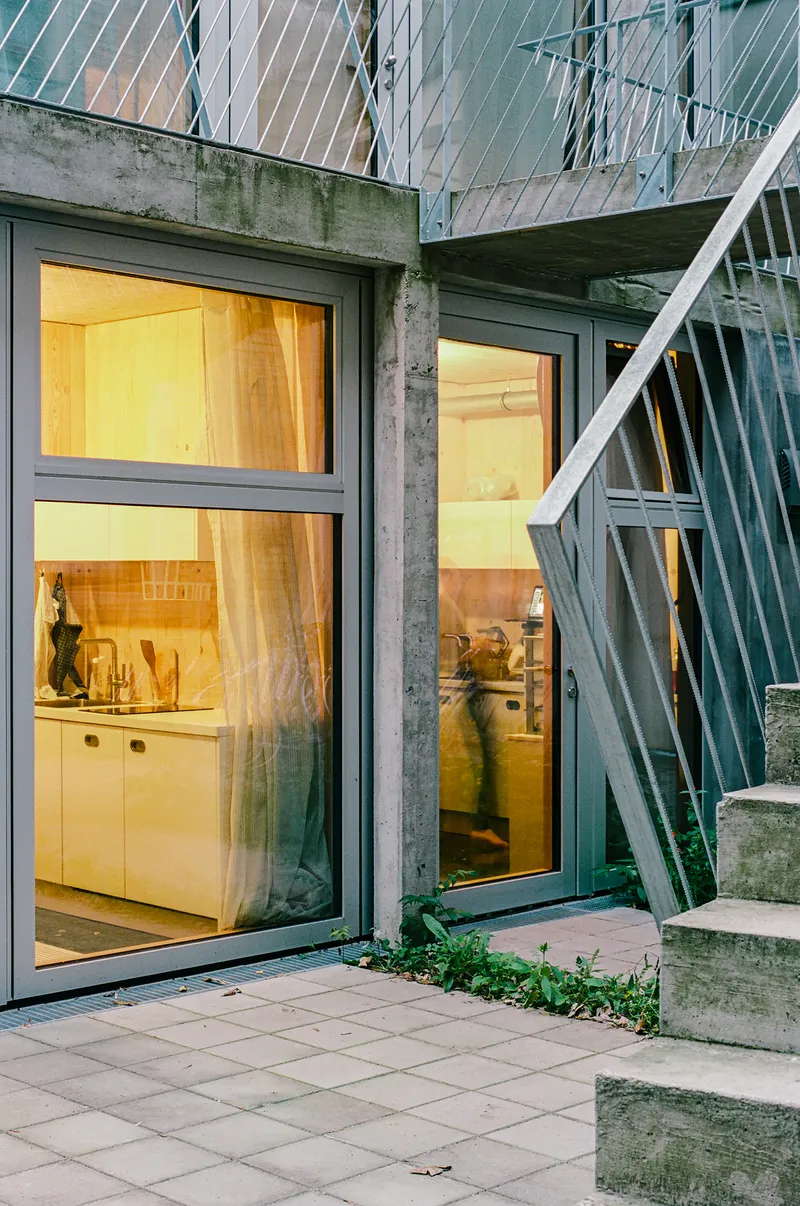 Glass sliding doors opening to a paved courtyard with illuminated kitchen visible inside at dusk