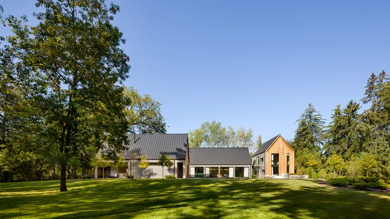 Three gabled volumes with metal and wood cladding arranged across a lawn beneath mature trees
